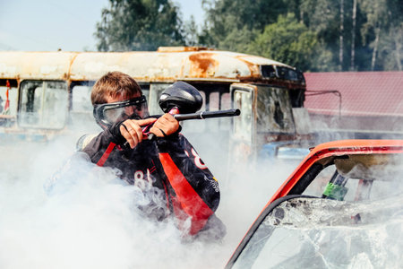 A paintball player who is ready to shoot from hiding.Paintball player in protective uniform and mask.の写真素材
