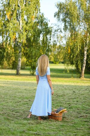 A young slender girl stands on the lawn with a basket containing a bouquet of lavender and French baguettes.の写真素材