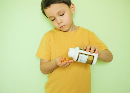 A little boy in a yellow T-shirt pours vitamins from a jar into his hand.の写真素材