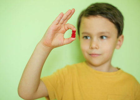 The child holds a red vitamins in his hand and looks at it.