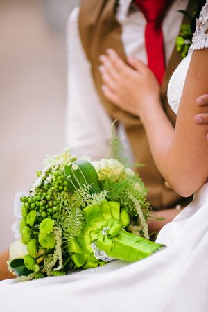 A modern, delicate white-green wedding bouquet lies on the brideâs knees. in the background, the brideâs hand gently touches the groom.の写真素材