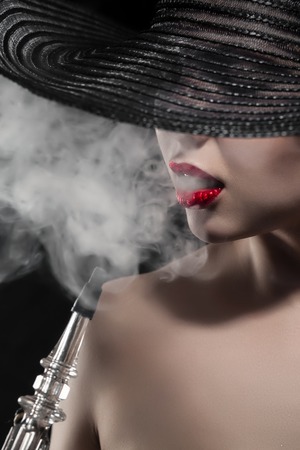 beautiful naked girl with red lips smokes hookah on black background; portrait of graceful hookah smoker womanの写真素材