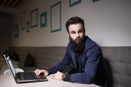 bearded man in suit and with laptop sitting in cafe and browsing internet;の写真素材
