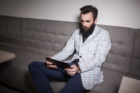 bearded man in suit and with tablet sitting in cafe and browsing internet;の写真素材