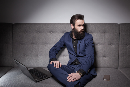 bearded man dressed in suit and with laptop browsing internet;の写真素材