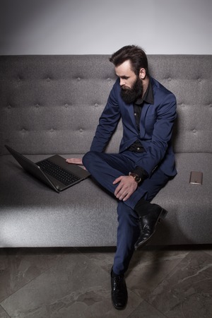 bearded man dressed in suit and with laptop browsing internet;の写真素材