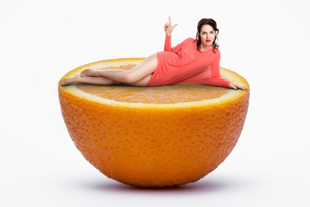 small female lying on half of giant orange; woman on diet,の写真素材