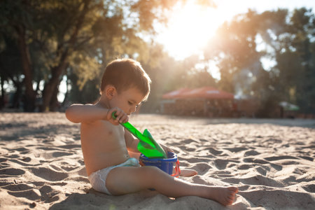 happy kid play with sand on beach; cheerful little boy have fun with shovel and bucket at river;の写真素材