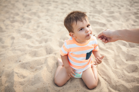 little boy eat icecream from mothers hand; mom feeding small kid with ice cream;の写真素材