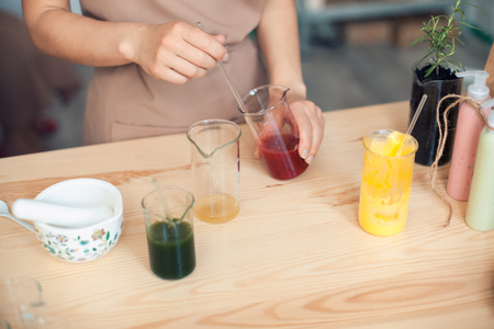 woman makes handmade cosmetics on wooden table; female prepare homemade creme with colorful ingredients;の写真素材