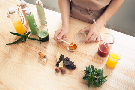 woman makes handmade cosmetics on wooden table; female prepare homemade creme with colorful ingredients;の写真素材