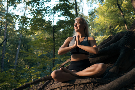 woman exercising pilates workout in forest in rays of sunshine;の写真素材