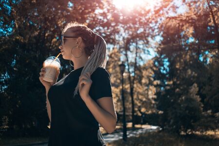 young beautiful braided female drinking milkshake with caramel in sunny parkの写真素材