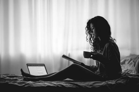 pretty brunette woman in morning bed with books and coffeeの写真素材