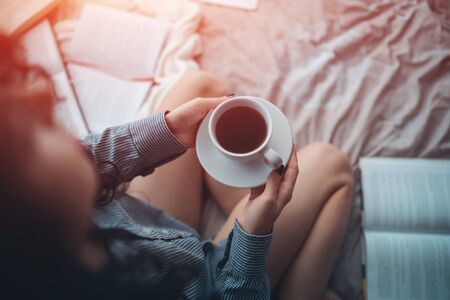 pretty brunette woman in morning bed with books and coffeeの写真素材
