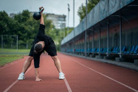 young athlete has workout and doing sport exercises with kettlebell outdoorの写真素材