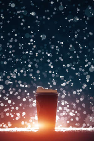 big paper cup with tea or coffee on falling snow background at nightの写真素材
