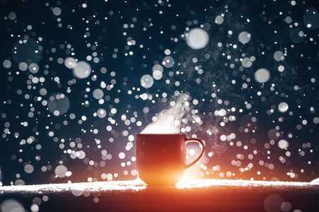 backlighted cup of hot steaming coffee drink or tea on night snowy backgroundの写真素材