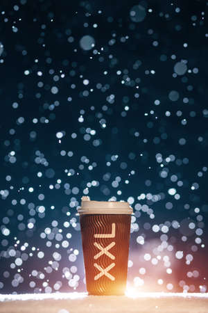 big paper cup with tea or coffee on falling snow background at nightの写真素材