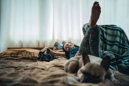 woman resting with couple of lovely french bulldog pets on bed at homeの写真素材