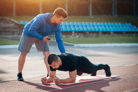 athletic sport man planking and exercising with fitness coach at stadiumの写真素材
