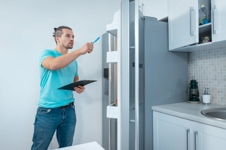 fitness nutritionist man with clipboard revising or look at fridge at kitchenの写真素材