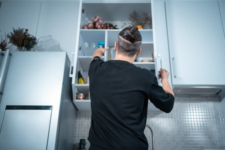 young attractive man open kitchen shelf with food to prepare eat at homeの写真素材