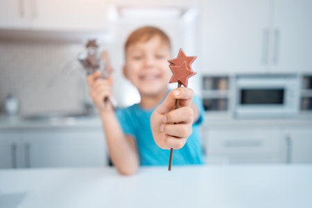 happy kid boy hold handmade sweets or candies on stick in hands at home kitchenの写真素材