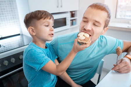 happy kid boy and father eating healthy peanut butter toast at home kitchenの写真素材