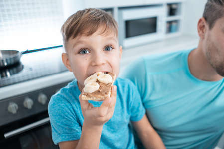 happy kid boy and father eating healthy peanut butter toast at home kitchenの写真素材