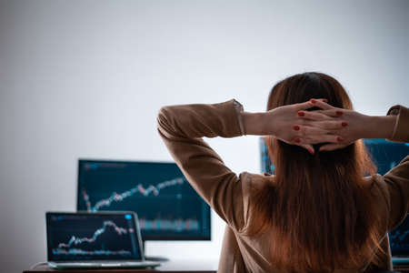 back view of female crypto trader resting and looking at monitor stock exchangeの写真素材