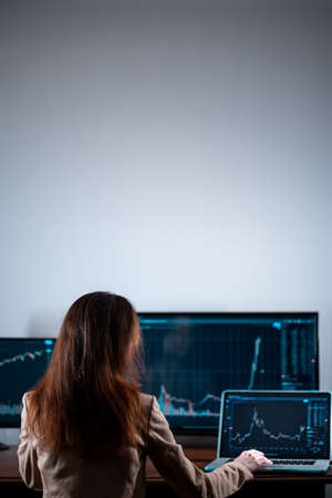 back view of female trader looking at monitor with stock exchange graph or chartの写真素材