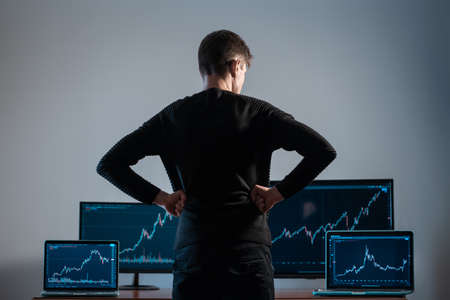 back view of male trader looking at monitor with stock exchange graph or chartの写真素材