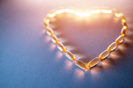 golden fish oil capsules omega 3 vitamins in heart shape on purple backgroundの写真素材