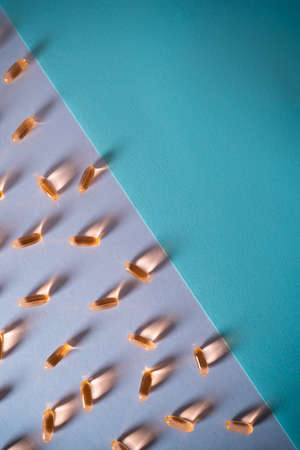healthy golden fish oil capsules omega 3 vitamins on purple and blue backgroundの写真素材