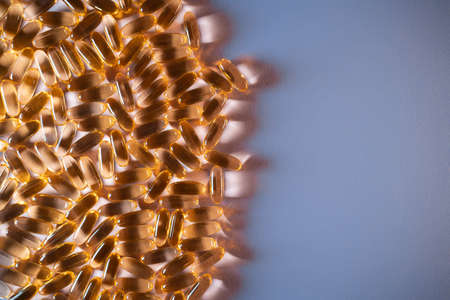 handful of golden fish oil capsules omega 3 vitamins on purple backgroundの写真素材