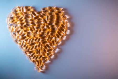 golden fish oil capsules omega 3 vitamins in heart shape on purple backgroundの写真素材