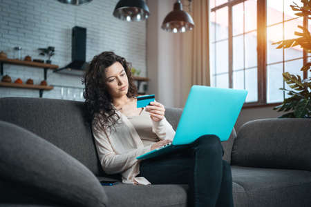 young female make online purchase with credit card and laptop on sofa at homeの写真素材