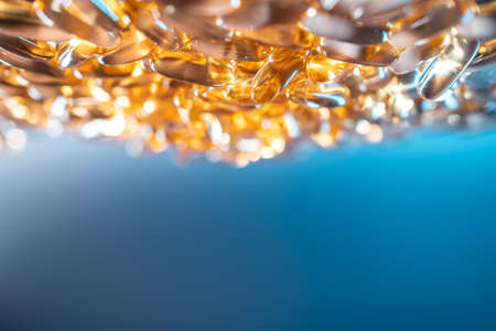 handful of golden fish oil capsules omega 3 vitamins on blue backgroundの写真素材