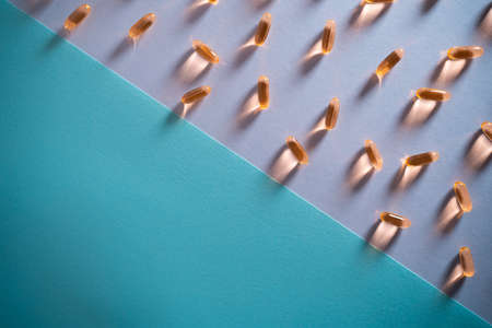healthy golden fish oil capsules omega 3 vitamins on purple and blue backgroundの写真素材