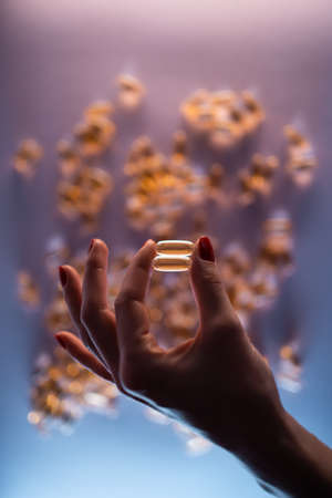 close up of hand holding fish oil capsule or omega 3 vitamins on blue backgroundの写真素材