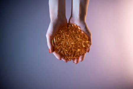 closeup of hands holding handful of fish oil capsules omega on purple backgroundの写真素材