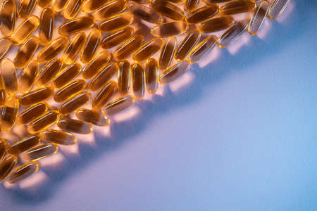 handful of golden fish oil capsules omega 3 vitamins on purple backgroundの写真素材