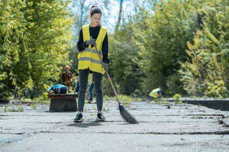 pretty volunteer female cleaning up park from dust waste and foliageの写真素材