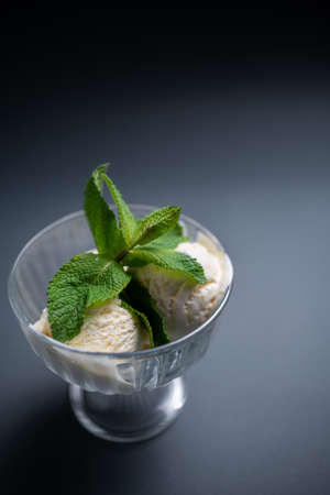 tasty vanilla ice cream with fresh mint in glass bowl on black backgroundの写真素材