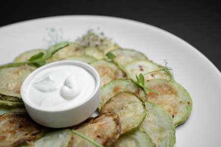 closeup of fried zucchini slices with sour cream on plate on black backgroundの写真素材