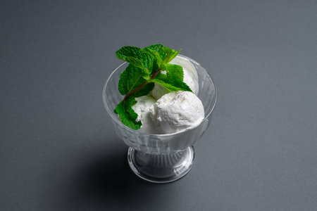 tasty vanilla ice cream with fresh mint in glass bowl on black backgroundの写真素材