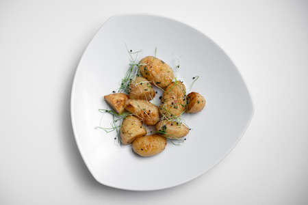top view of tasty roasted potatoes with microgreen on plate on white backgroundの写真素材