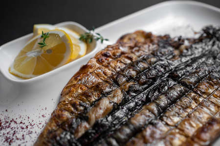 closeup of grilled mackerel fish with lemon on white plate on black backgroundの写真素材