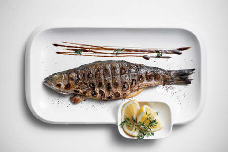top view of whole grilled stuffed fish with lemon on plate on white backgroundの写真素材
